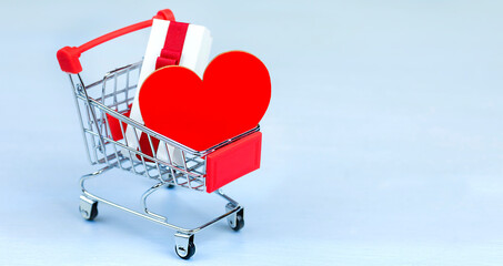 Shopping basket on a blue wooden table. A gift box with a red ribbon and a bright red heart. Close-up.