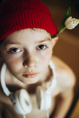 Cute Hipster Teenage boy with white tulip flower on ear in red knitted hat and white headphones