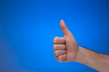 Thumb's up like gesture made by Caucasian male hand. Close up studio shot, isolated on blue...