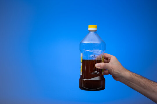 Spent Cooking Oil Recycling In A Clear Plastic Bottle. Held In Hand By Man. Close Up Studio Shot, Isolated On Blue Background