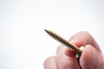 Small metal threaded screw held by Caucasian male hand between fingers. Close up studio macro shot, isolated on white background