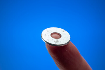 Very small metal washer held between fingers by man. Close up macro studio shot, isolated on blue background