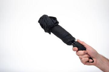 Folded and closed black fabric umbrella held in hand by man. Close up studio shot, isolated on...