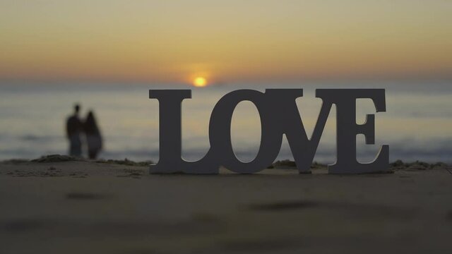 Letter Love on the sea sand sunset background. 