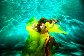 Girl in a beautiful dress under blue water. Female model posing under water in swimming pool - obrazy, fototapety, plakaty
