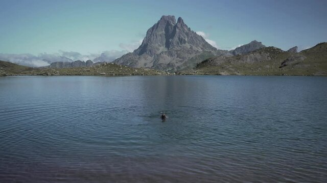 View of a young lady swimming in the pristine blue lake Ayous on a bright sunny morning with the view of mountain range in the background Pyrenees in France.