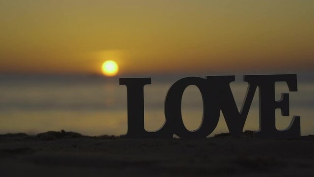 Letter Love on the sea sand sunset background. 