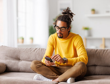 Young focused serious african american man relaxing at home with smartphone, surfing internet
