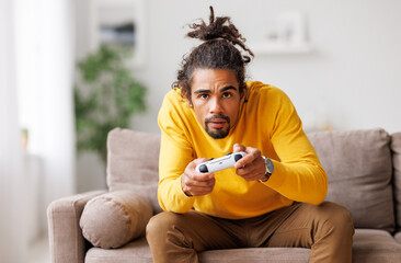 Young positive happy african american guy with wireless gamepad playing video game at home