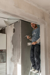 Fototapeta premium A man-a master of European appearance plasters the walls, makes repairs in the apartment, the concept of repairing and remodeling the house