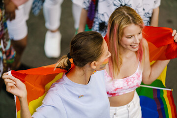 Young lesbian couple walking with rainbow flag during pride parade