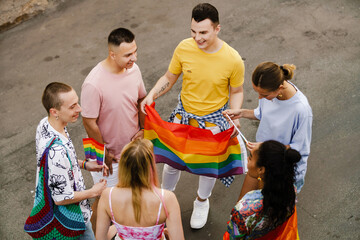 Young gay people smiling and holding rainbow flags during pride parade