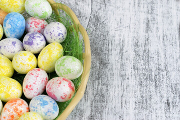 On a wooden table is a wicker basket with dyed eggs and sparkles. Easter