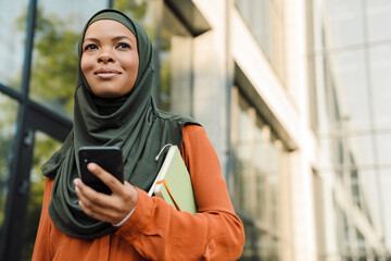 Black muslim woman using mobile phone during walking