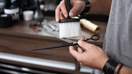Detail of professional barber cleaning scissor with soft brush at barber shop.