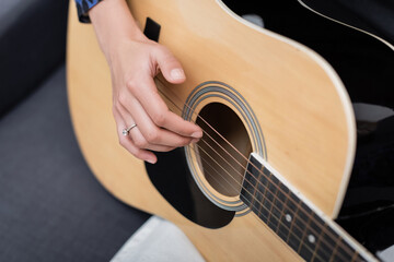 Fototapeta premium Cropped view of african american woman playing acoustic guitar on couch.