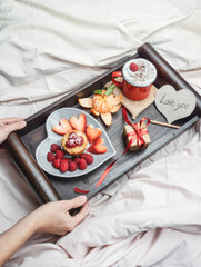 Breakfast in bed. Woman holds breakfast tray with berries, heart, coffee cup, cappuccino, strawberries and raspberries, tangerine and a gift. Morning surprise. Valentine's Day. Honeymoon.