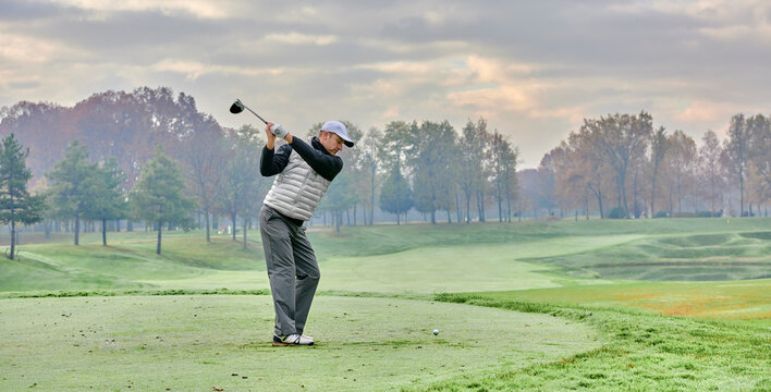 Golfer on a golf course in winter with fog and frost, on the starting tee. Golfer with golf club hitting the ball for the perfect shot.