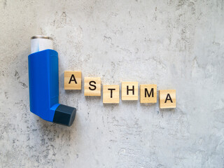 Top view of a blue inhaler and the inscription "asthma". The word is made of wooden letters.