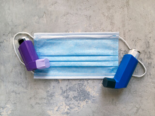 Top view of purple and blue inhalers lying on a surgical mask. Medical theme.