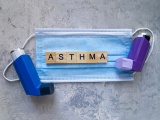 Top view of a medical face mask and two asthma inhalers. The word asthma composed of wooden letters.