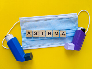 Top view of a blue surgical mask and two inhalers on a juicy yellow background. The word ASTHMA...