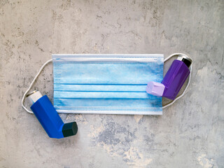 Top view of blue and purple asthma inhalers lying on a medical face mask. Medical theme.