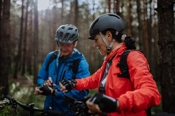 Senior couple bikers setting smartwatch outdoors in forest in autumn day.