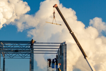 Builders standing on a monolithic building under construction against a blue sky. Construction crane copy space