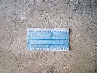 Top view of one blue surgical mask on a gray background. Personal protective equipment.