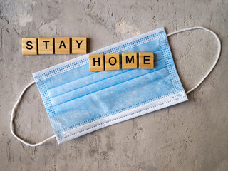 Words STAY HOME lined with wooden letters on a background of blue surgical masks.