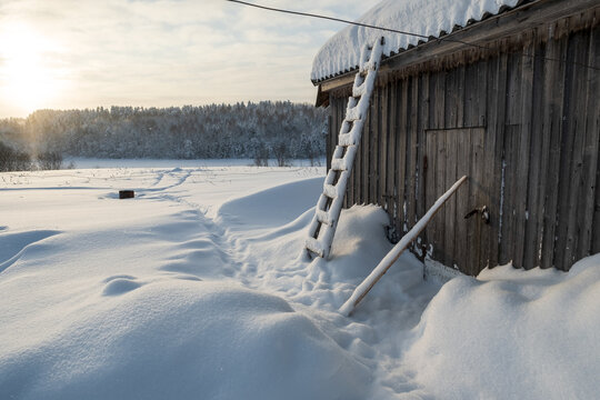 Wonderful winter rural landscape. Old wooden barn, against the backdrop of a snowy meadow and forest, at sunset.