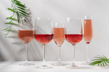 Set of rose wine or champagne in variety of glasses on white background with shadows and palm leaves. Romantic party, vacation, holiday concept