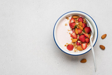 Strawberry yogurt with fresh berries, homemade granola, almonds in bowl. Healthy breakfast on light background
