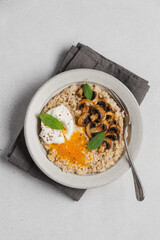 Savory oatmeal with poached egg, fried mushrooms. Healthy morning breakfast served in ceramic plate on gray background, top view with copy space