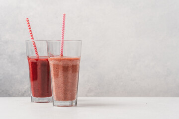 Strawberry smoothie in tall glasses with paper tubes on light gray background