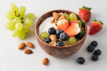 Greek yogurt with berries and granola in wooden bowl. Healthy breakfast with strawberries, grapes, blueberries, oatmeal and almonds