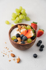 Greek yogurt with berries and granola in wooden bowl. Healthy breakfast with strawberries, grapes, blueberries, oatmeal and almonds