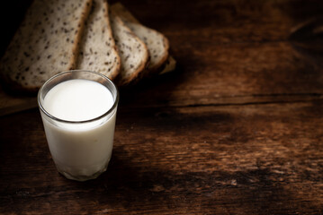 A full glass of milk. Bread in the background is blurred. Dark wooden background. Morning breakfast. Rustic style