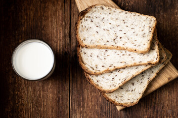 A full glass of milk. Bread in the background is blurred. Dark wooden background. Morning breakfast. Rustic style
