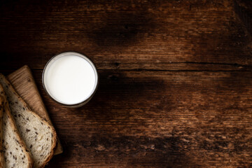 A full glass of milk. Bread in the background is blurred. Dark wooden background. Morning breakfast. Country style. Place for your text.
