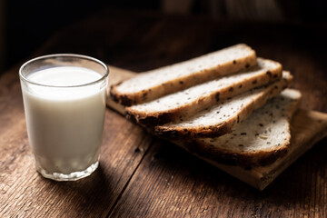 A full glass of milk. Bread in the background is blurred. Dark wooden background. Morning breakfast. Rustic style
