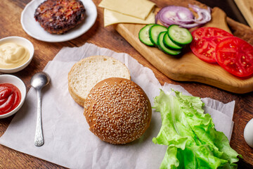 Ingredients for a classic hamburger. Grilled meat, vegetables, greens, sauces near a sesame bun. Wooden background. Cooking hamburger or cheeseburger.