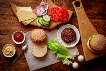 Ingredients for a classic hamburger. Grilled meat, vegetables, greens, sauces near a sesame bun. Wooden background. Cooking hamburger or cheeseburger.