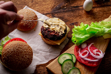Fototapeta na wymiar Ingredients for hamburger, cheeseburger. Wooden background. The hamburger is smeared with sauce. Cooking. Hamburger day.