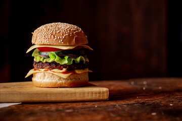 Hamburger with grilled meat cheese, green salad and tomato. Wooden background. Hamburger Day.