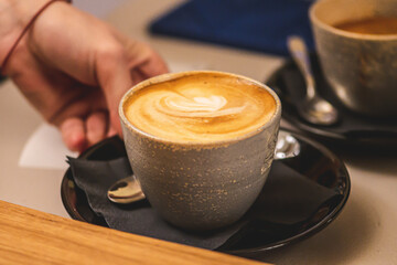Cup of cappuccino with foam served by the hand of a girl at a bar counter, one in a ceramic mug, one in a glass