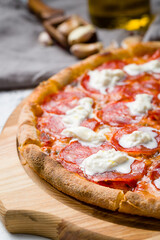 pepperoni pizza with strachatella cheese on wooden board on grey table macro close up
