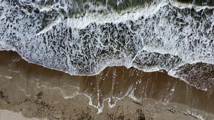 Aerial drone view flight over sea waves that roll onto sandy shore. Top view. Waves with white foam...