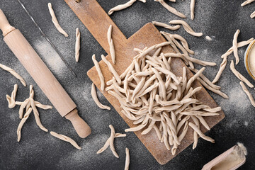 Whole grain wheat apulian pasta Pizzarieddi or maccaruni on a cutting board on black table. Fresh maccheroni typical dish of Puglia, Salento Italy. Italian homemade pasta background, copy space